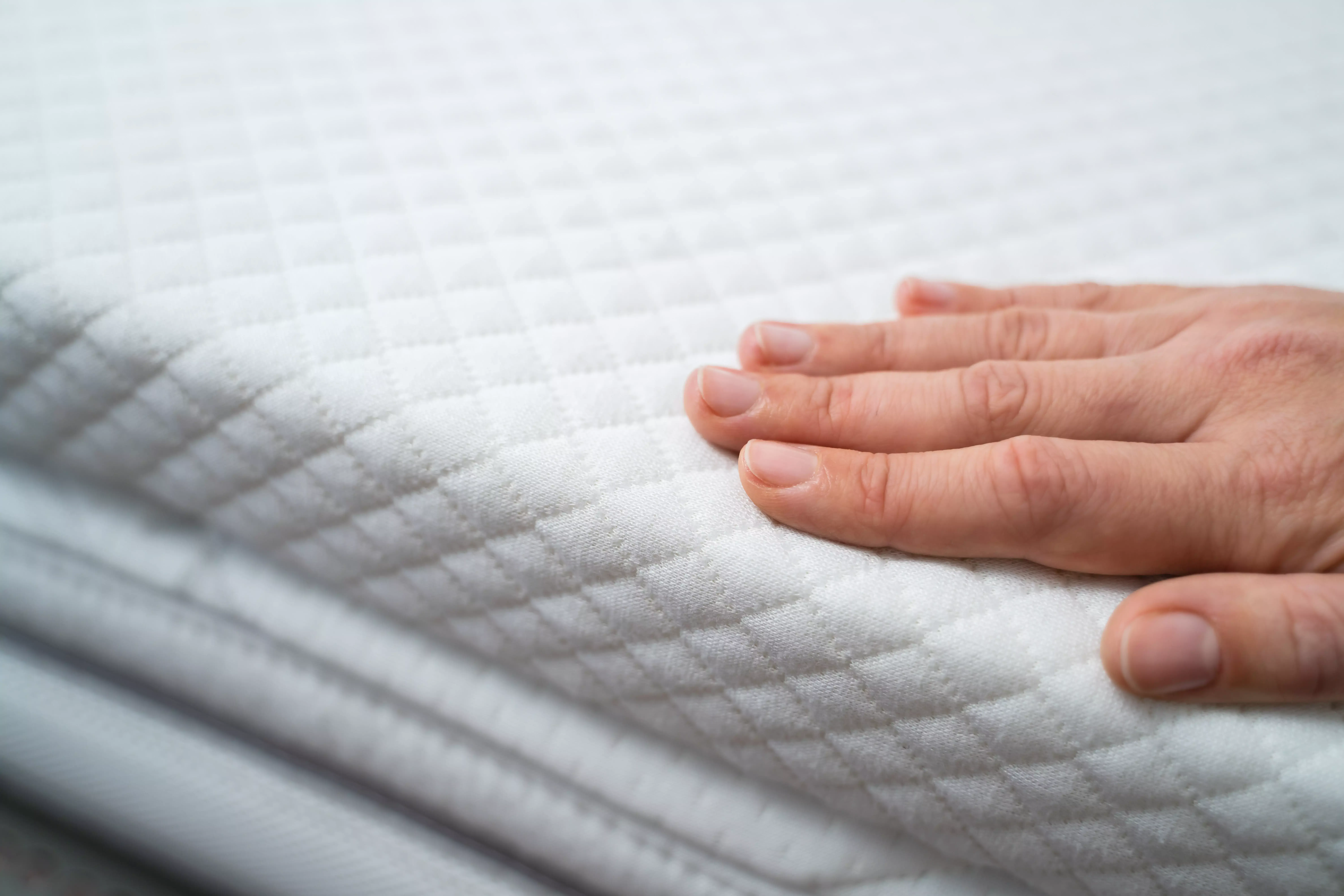 La mano presiona suavemente sobre la superficie de un topper acolchado - revela la superficie suave y texturizada para un sueño confortable.